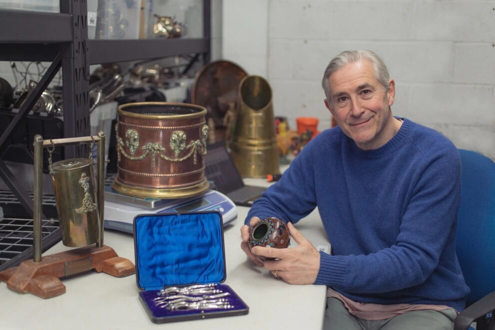 man surrounded by vintage silver and antique items